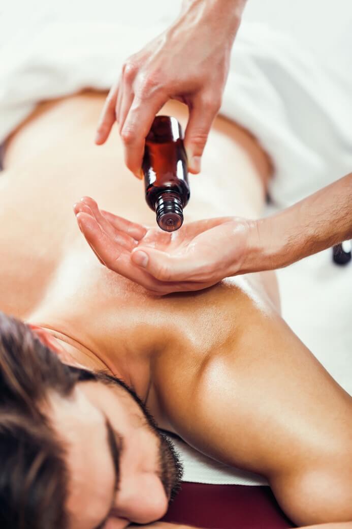 A woman with closed eyes rests her head on her hands on top of a white Hand & Stone towel as someone massages her shoulders 