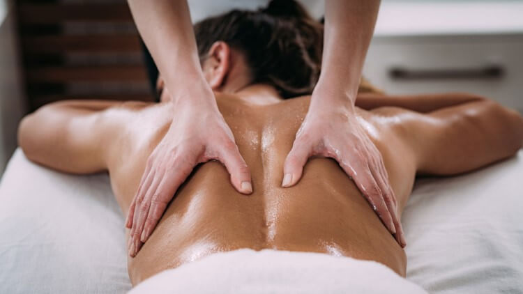 A man with his eyes closed lying on his stomach resting his head on his hands while someone‘s hands massage his back